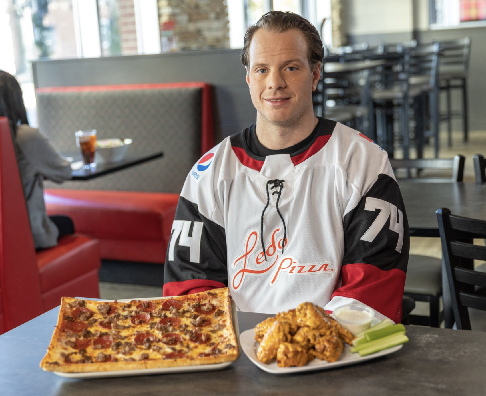 John Carlson Sitting at table with pizza and wings.