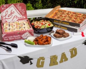 Catering spread for graduation with catering sub platter, 12 wings, catering sized salad, brownies, and 2 18" meatlovers pizzas.
